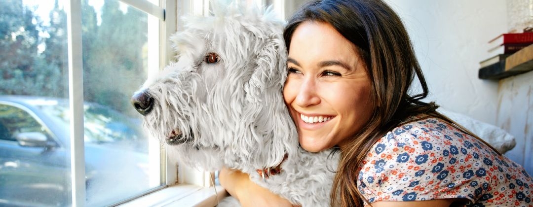 A woman hugging her dog while looking through the window