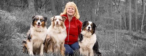 Smiling woman with three dogs in an outdoor setting, highlighted by selective color.